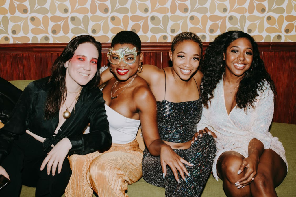 Four friends sitting together on a couch, smiling at the camera and dressed for a night out, showcasing friendship, diversity, and social connection.