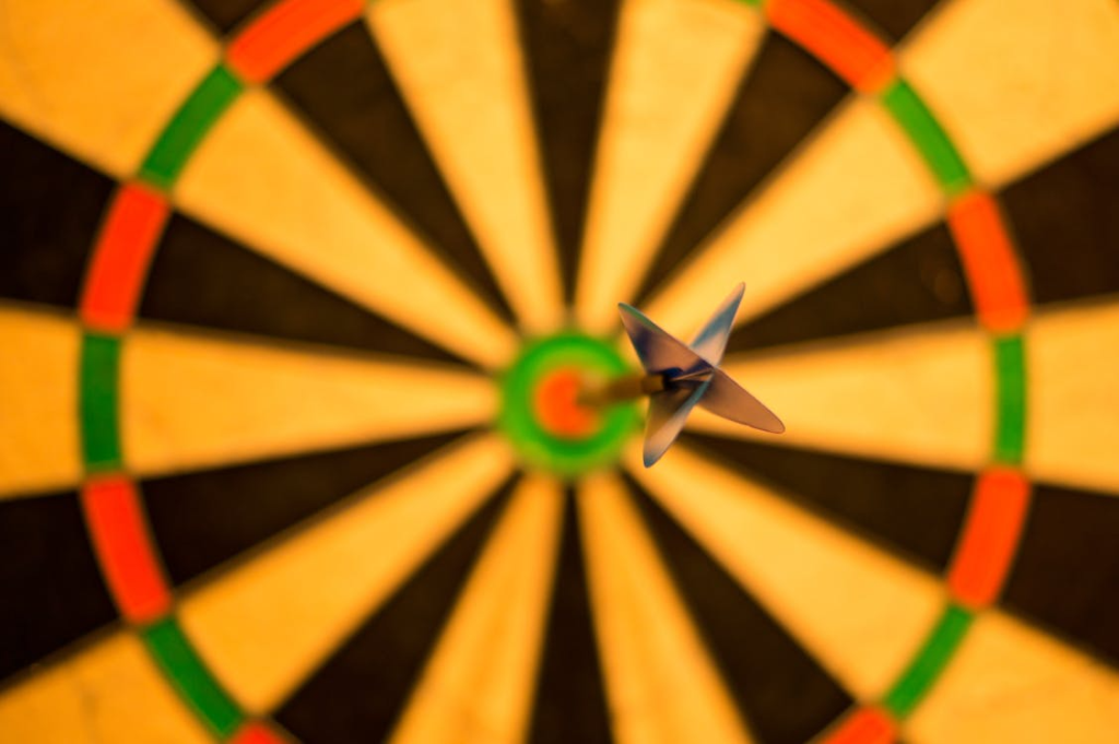 Close up of a dart hitting the bullseye on a dartboard, symbolizing goal achievement, business strategy success, target marketing, focus, and precision planning.