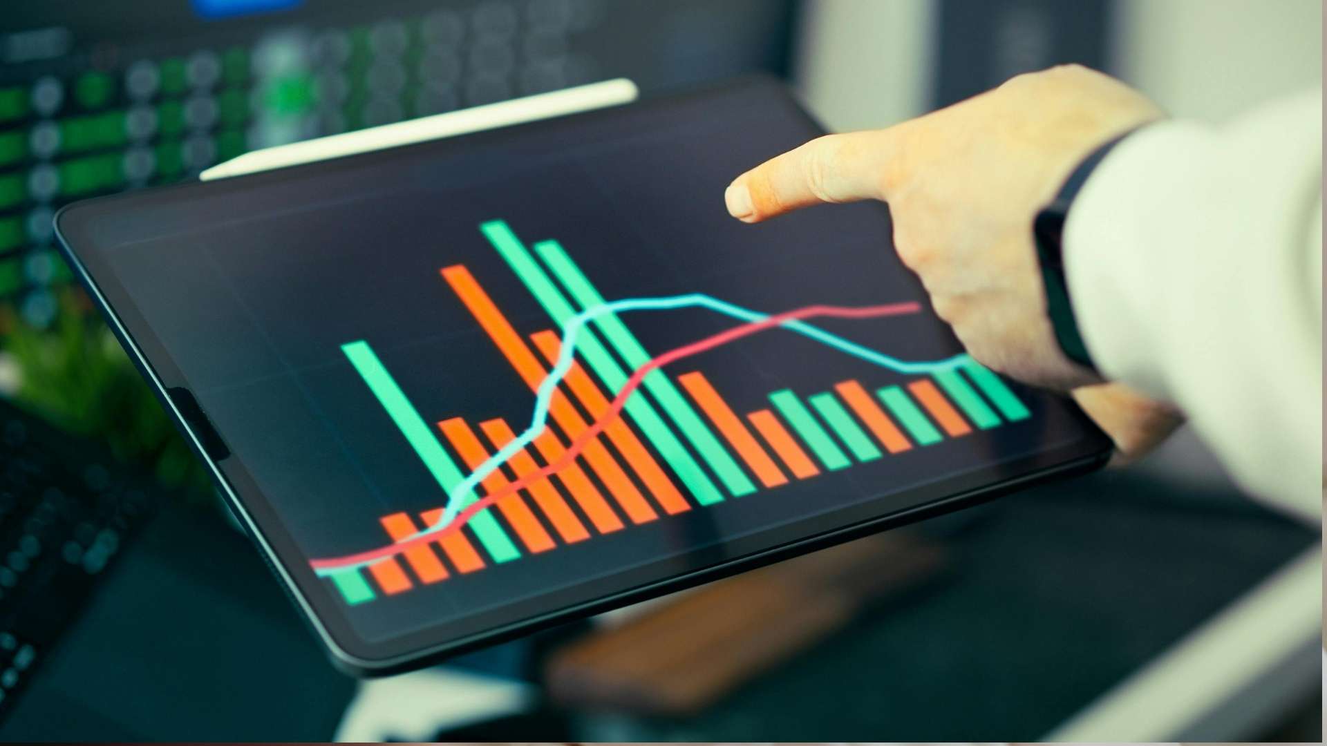 Person pointing at a tablet screen displaying colorful bar and line charts for performance analysis