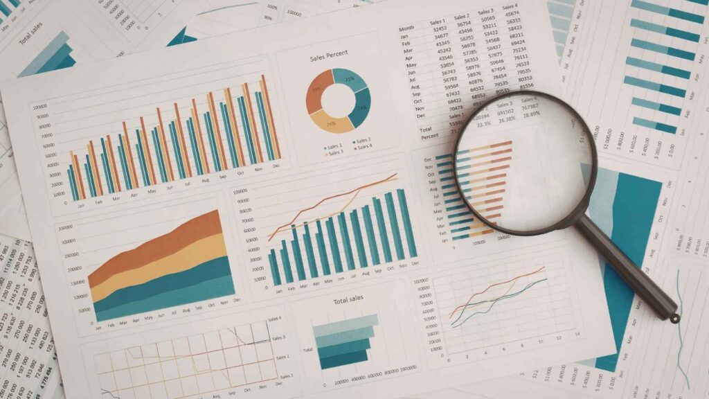 Business charts and sales graphs spread across a desk with a magnifying glass highlighting performance data