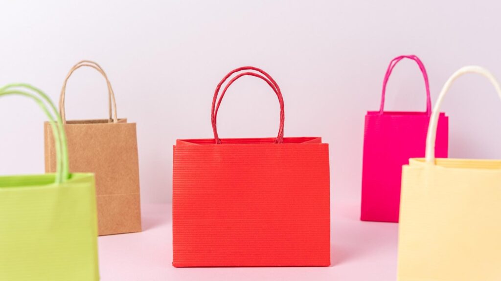 Colorful paper shopping bags arranged against a soft pastel background
