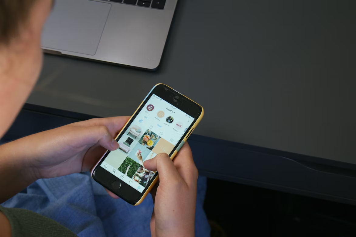 Person browsing Instagram feed on a smartphone while using social media at a desk with a laptop nearby