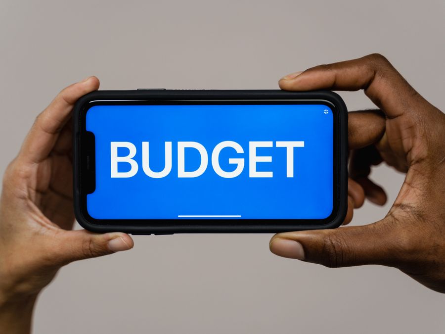 Two hands hold a smartphone displaying the word 'budget' on a blue screen, symbolizing financial planning.