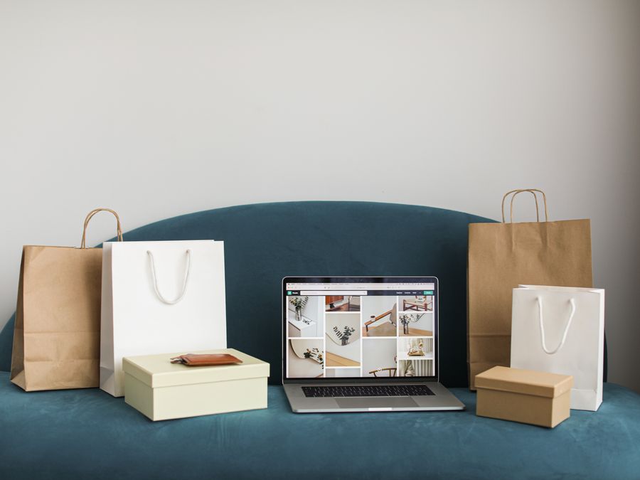 A laptop surrounded by shopping bags and boxes on a blue sofa, ideal for online shopping themes.