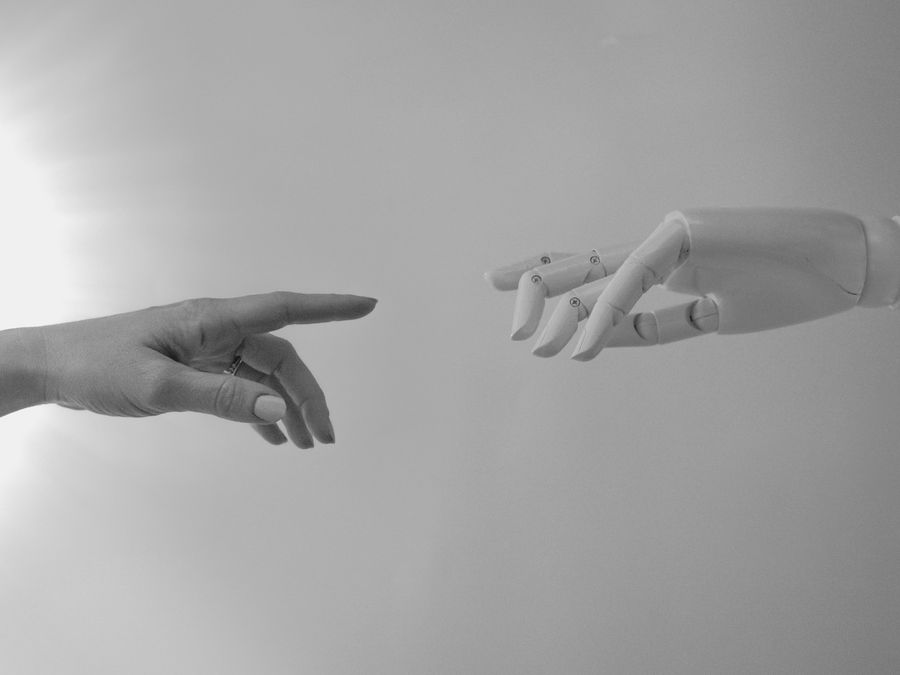 Black and white image of a human and robotic hand reaching towards each other, symbolizing connection.