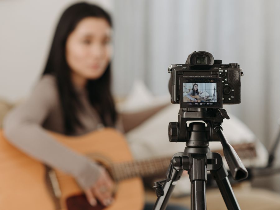 A woman plays guitar while recording a video indoors. Ideal for vlogs or music-related content.