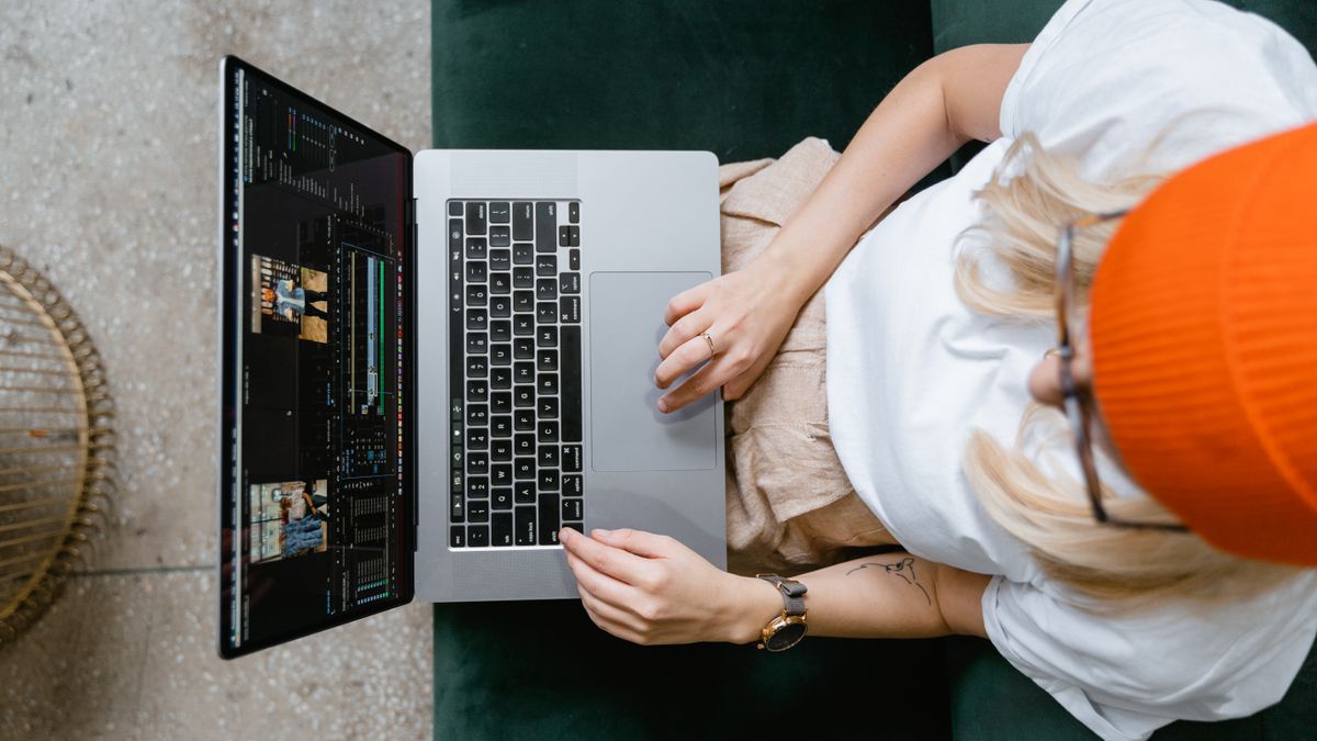 Top view of a woman editing video content on a laptop, wearing a casual outfit and orange beanie.