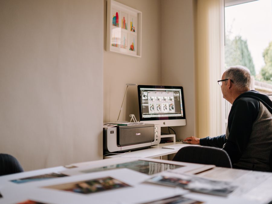 Elderly man engaged in photo editing at home office, showcasing a cozy and focused workspace.