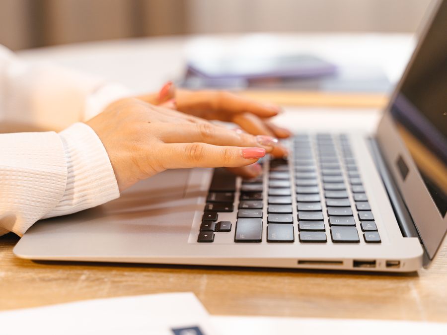 A close-up view of hands typing on a laptop keyboard with a focus on manicured nails and technology.