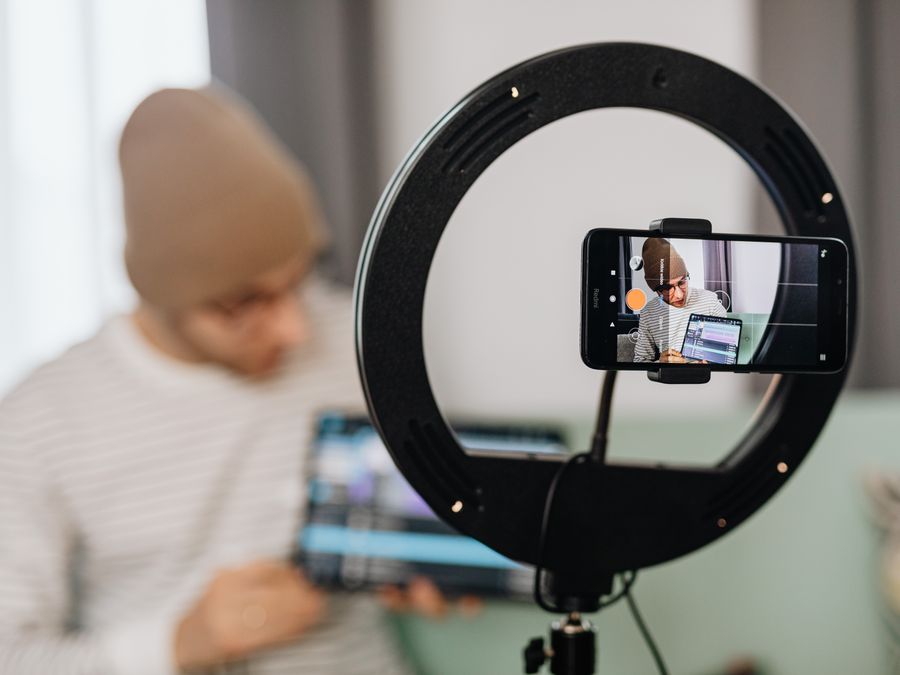 Man vlogging with a smartphone and ring light, focused on content creation indoors.