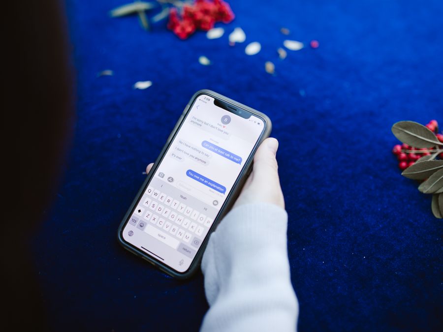 A person holding a smartphone displaying text messages on a blue surface with flowers.