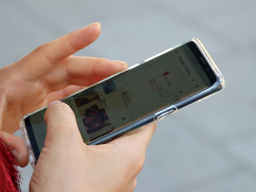 Hands holding a smartphone with a clear case, browsing a map outdoors.