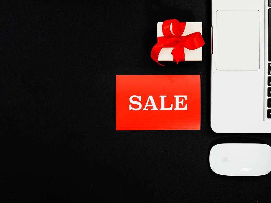 Flat lay of a laptop, gift box, and sale sign for online shopping promotion.