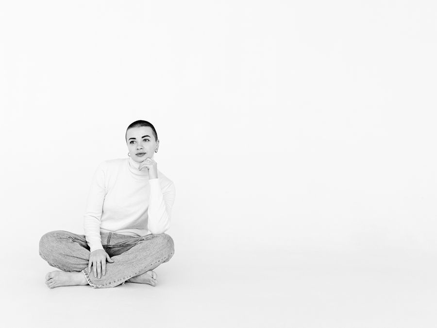Elegant minimalist black and white photo of a woman sitting in a studio setting, exuding calm and confidence.