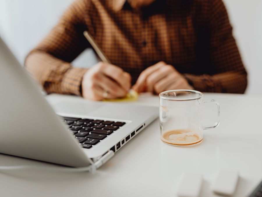 Close-up of a person writing with a notebook and a glass cup on a desk.