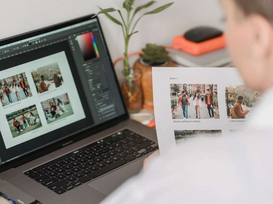 High angle of crop female photographer sitting at table with laptop and printed photoshoot while working remotely
