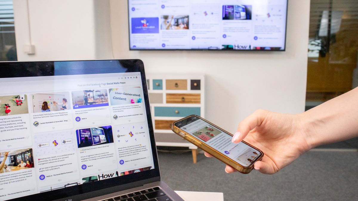 Person using smartphone and laptop in a modern office environment with digital screens.