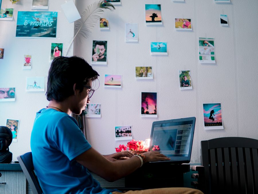 A man working on a laptop in an artistic workspace filled with photos and decor.