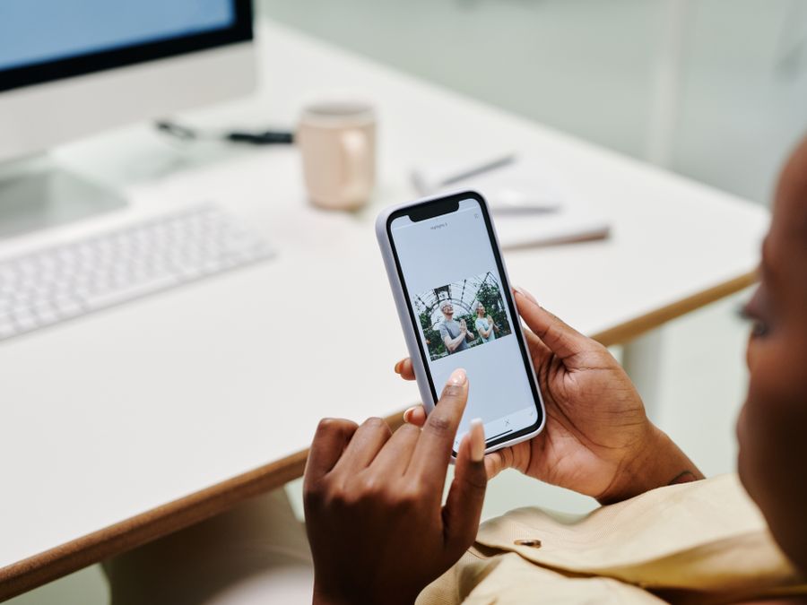 Close-up of hands using a smartphone at a desk with a computer. Ideal for tech and lifestyle content.