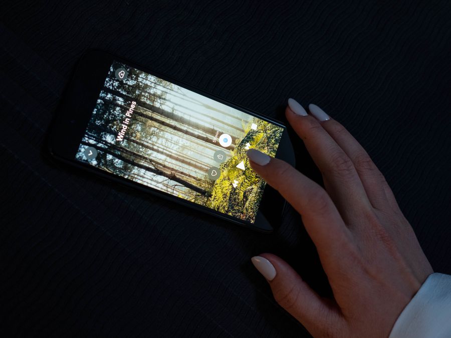 A hand interacting with a smartphone displaying a forest-themed app on a dark surface.
