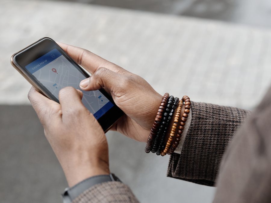 Close-up of hands with bracelets navigating on smartphone using GPS app outdoors.
