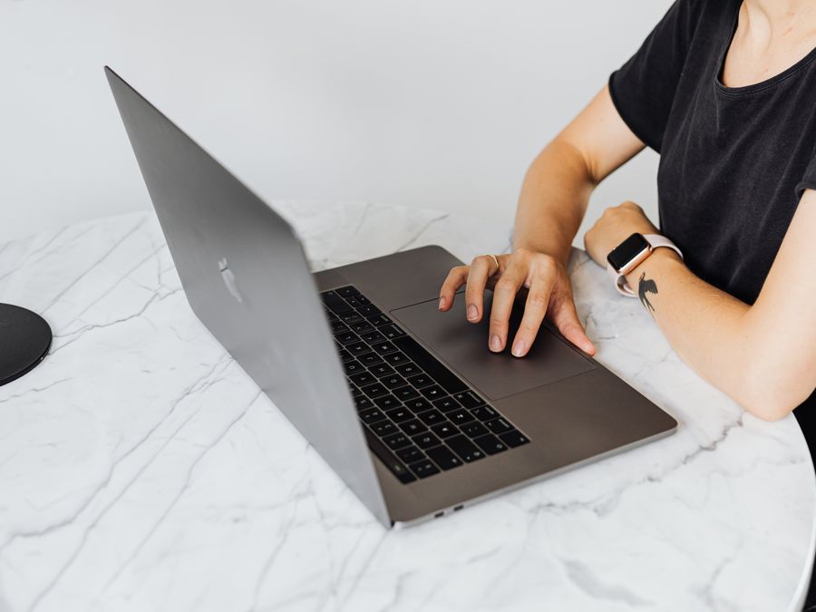 Person using laptop with smartwatch on marble table, showcasing modern technology.