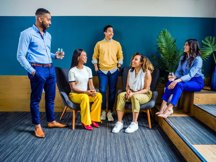 A diverse group of five professionals engaging in a casual indoor meeting, smiling and talking.