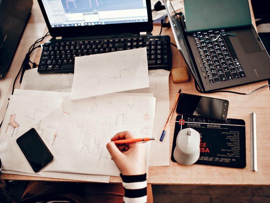 Top view of a business workspace with sketches, laptops, and drawing tools.