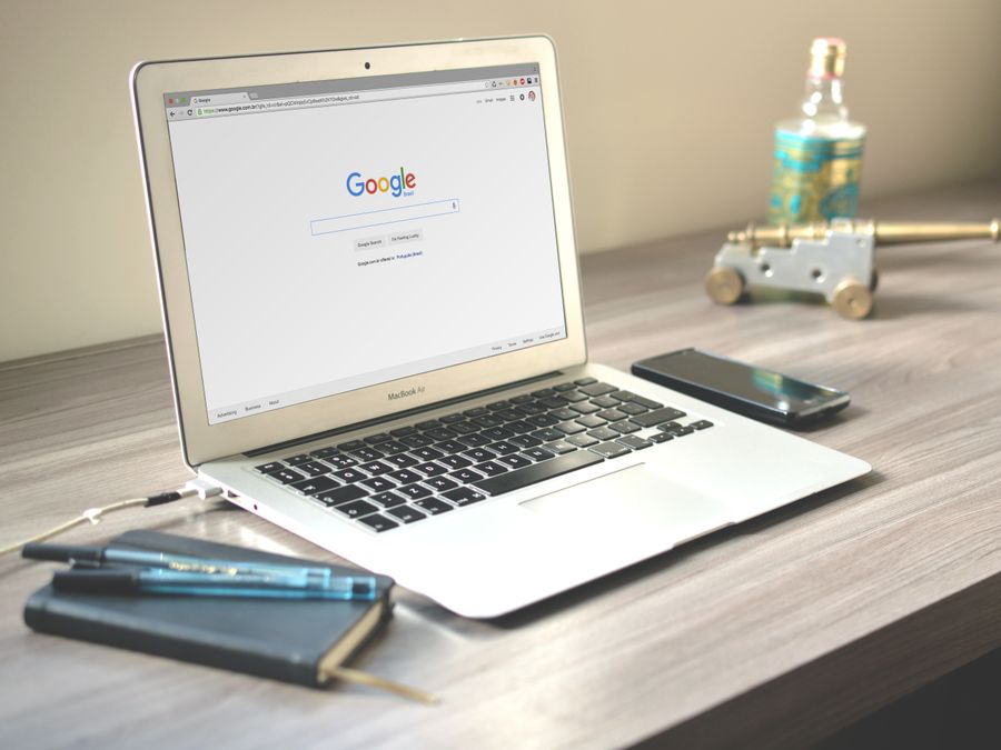A neat workspace featuring a laptop displaying Google search, a smartphone, and a notebook on a wooden desk.