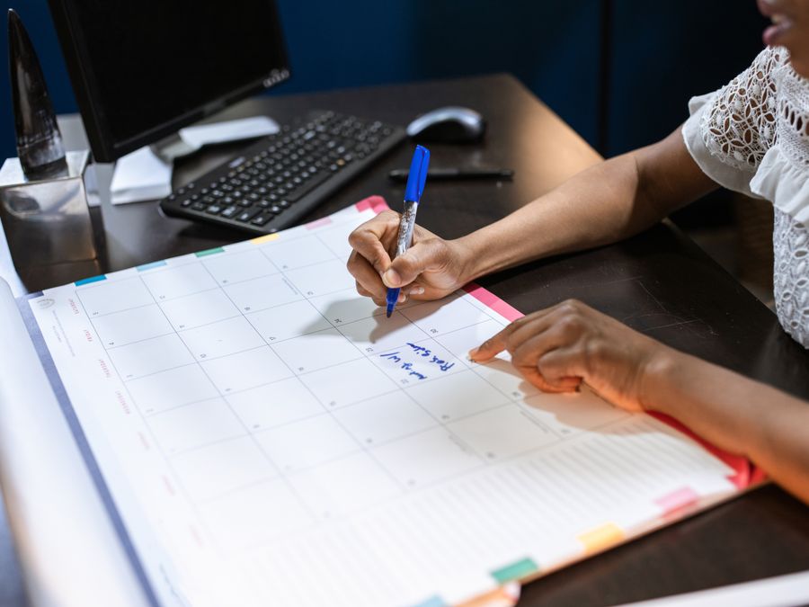Person writing important notes in a desk calendar with a pen, set in an office.