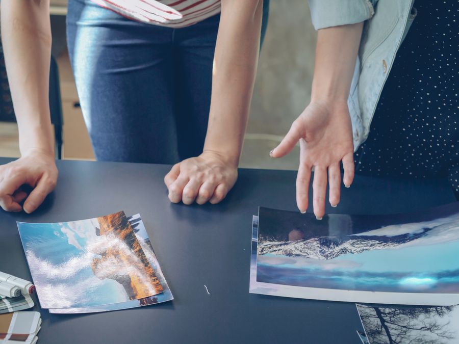 Two people analyzing printed landscape photographs on a table indoors.