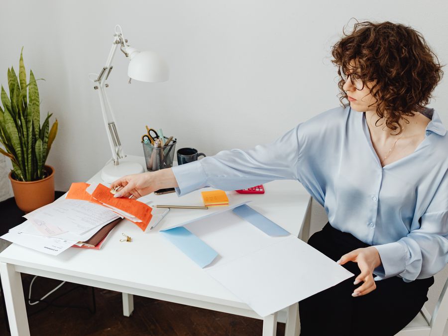 A woman organizing papers at her desk, working in a bright office environment.