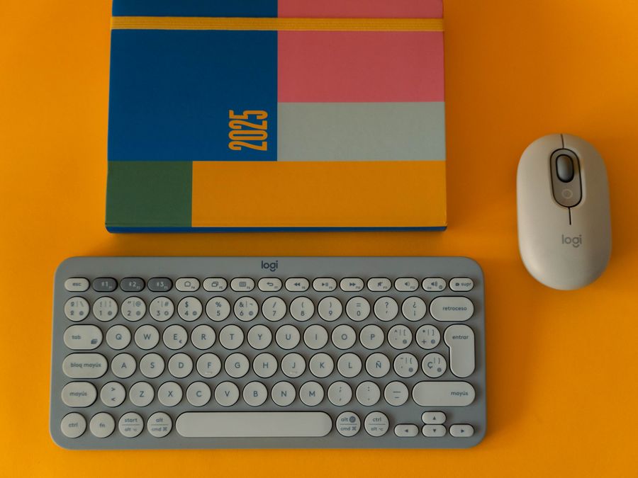 Flat lay of a colorful 2025 planner with keyboard and mouse on a bright orange background.