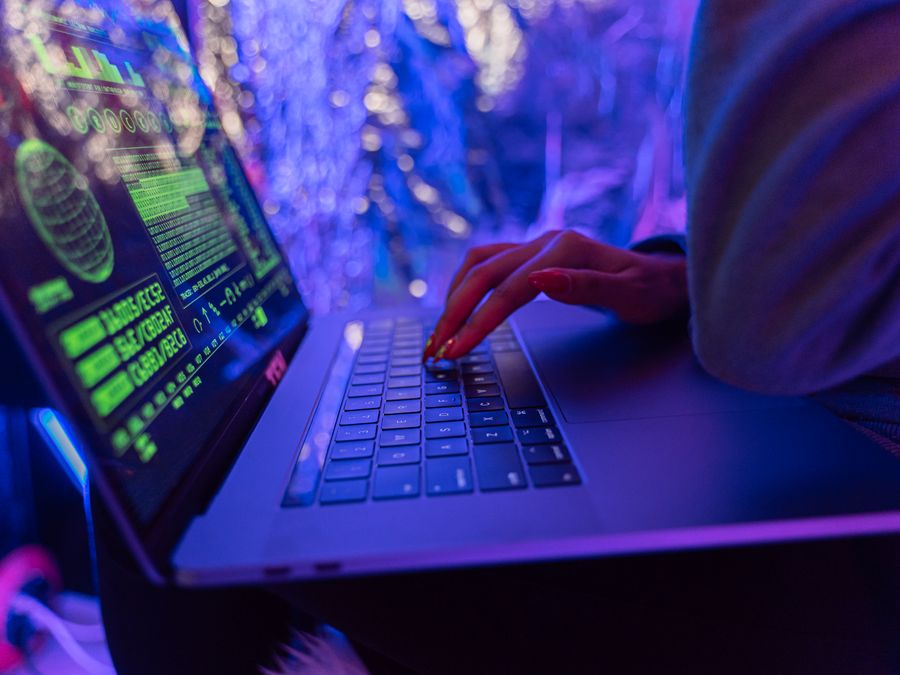 Close-up of hands typing on a laptop displaying cybersecurity graphics, illuminated by purple light.