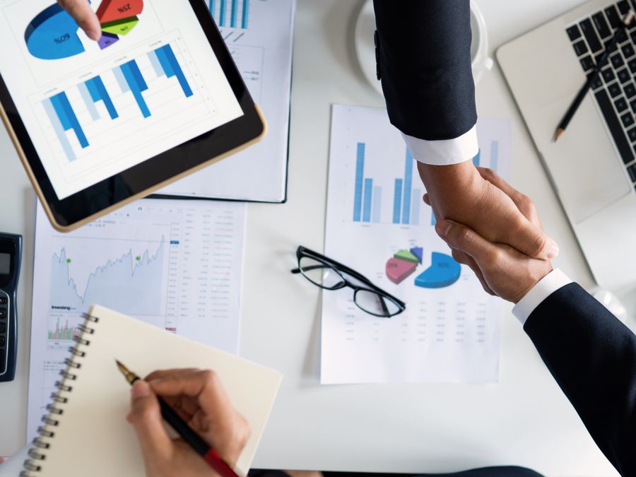 Business professionals handshake over graphs and charts in a corporate setting, symbolizing successful negotiation and agreement.