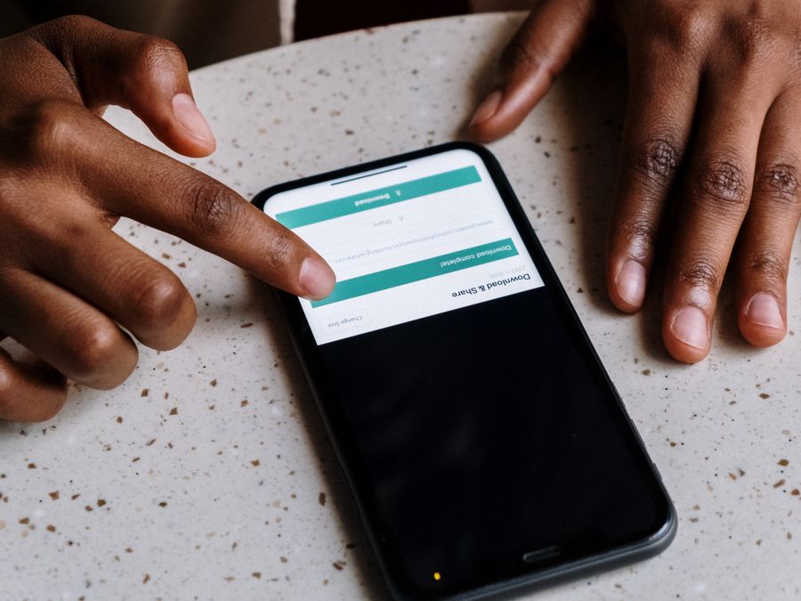 Close-up of hands interacting with a smartphone, displaying downloading interface.