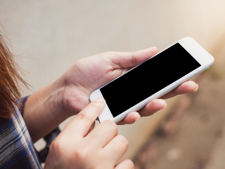Person holding and using a smartphone outdoors, focusing on hands and screen.
