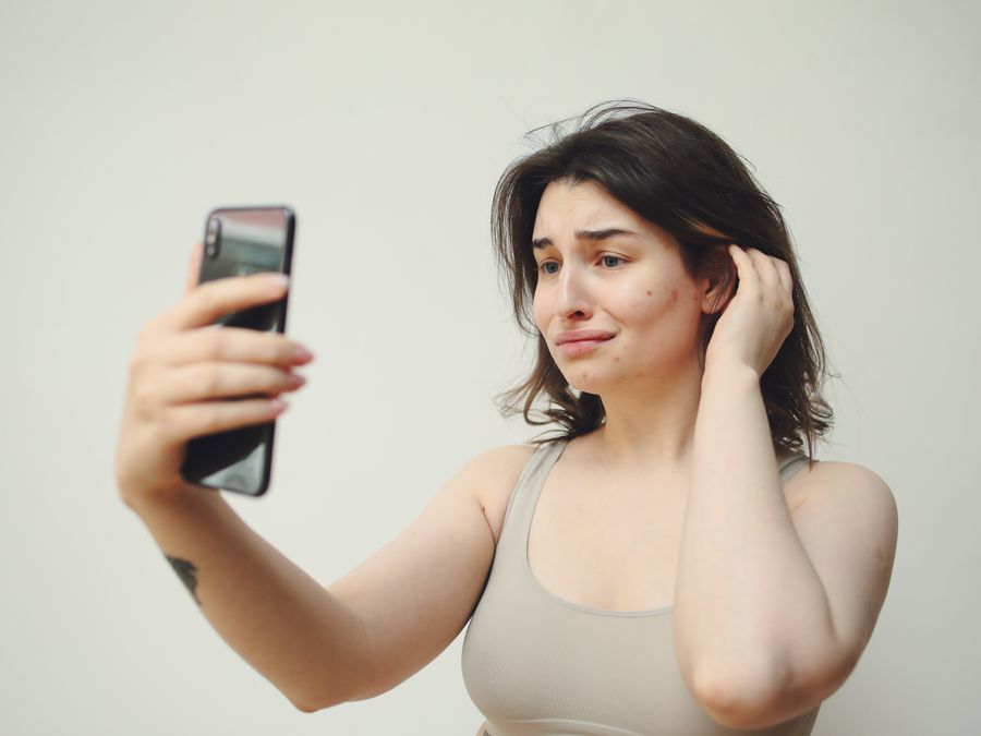 A young woman in a tank top taking a selfie with a worried expression on her face.