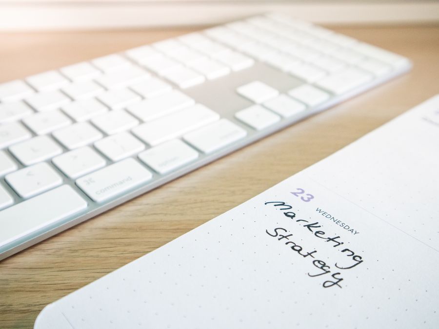 Notebook with marketing strategy note alongside a keyboard on a wooden desk.