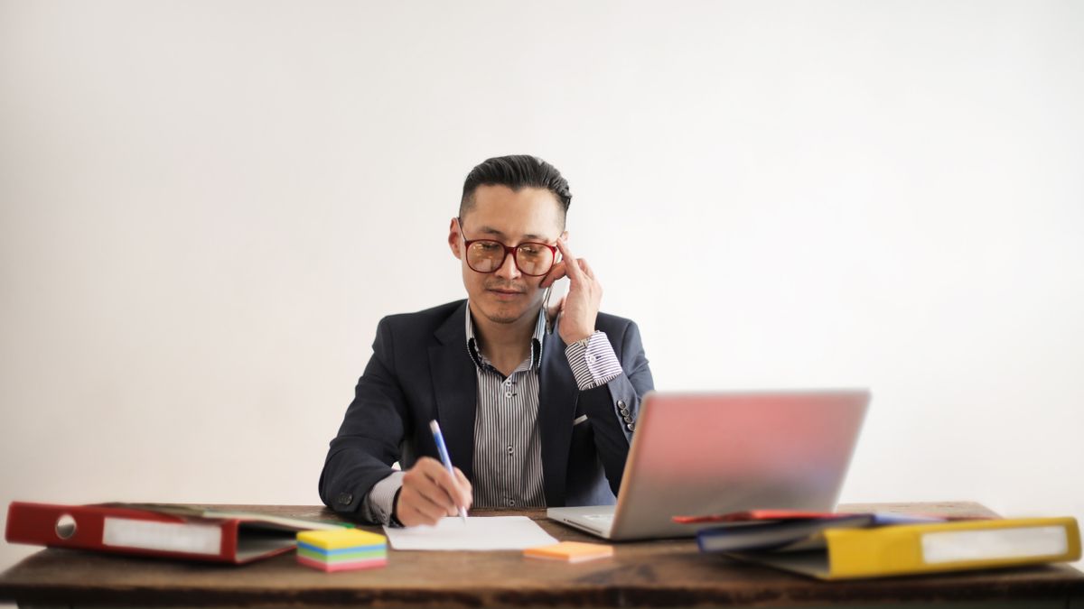 Focused businessman multitasking at desk, engaged in a phone call and working on a laptop.