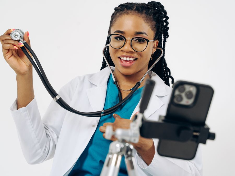 Young female doctor smiling while recording with smartphone and stethoscope.