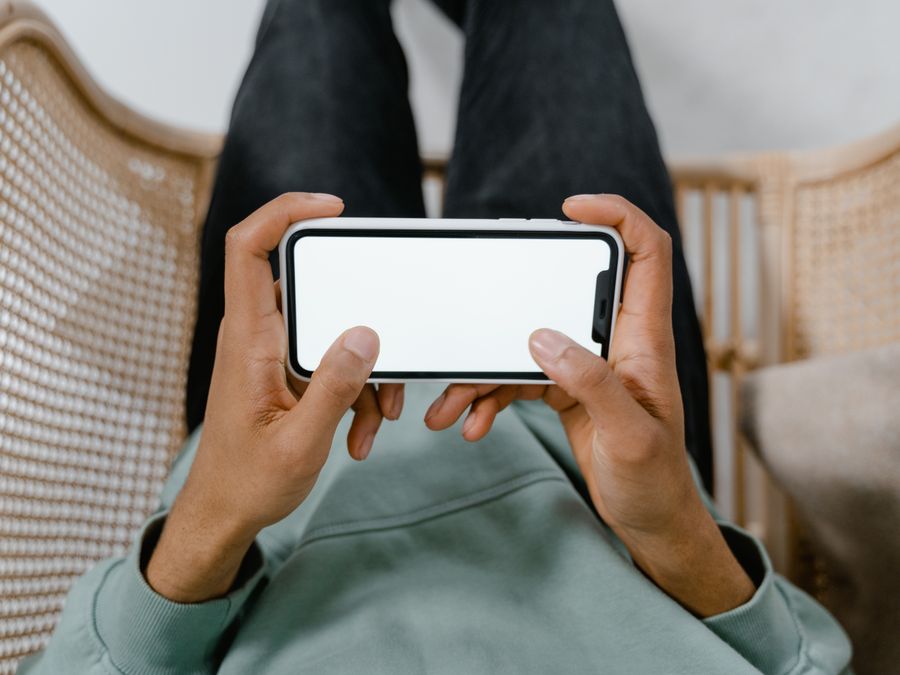 A person holding a smartphone with a blank screen while relaxing in a chair.