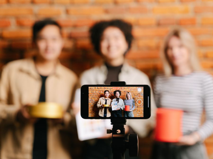 A diverse team of vloggers recording a video with a smartphone against a brick wall backdrop.