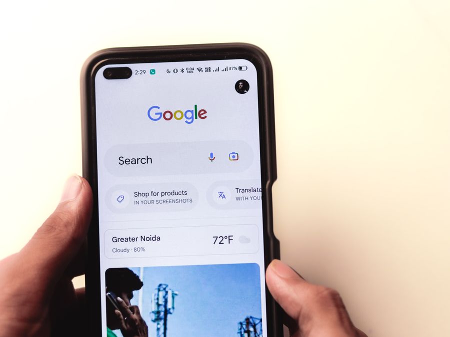 A close-up of a hand holding a smartphone with Google search displayed on the screen.