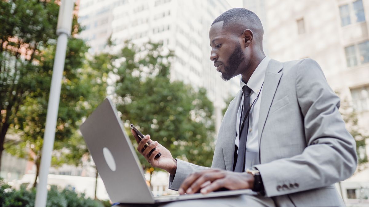 Businessman in a suit using a laptop and smartphone in an urban setting, blending technology with business.