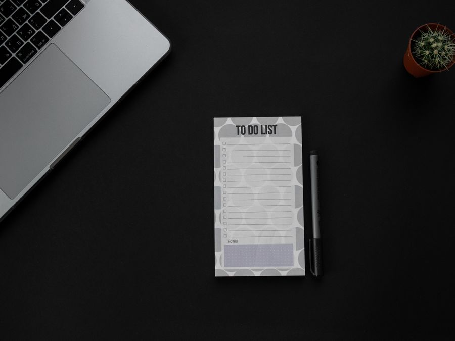 A minimalistic desk setup featuring a laptop, to-do list, and pen on a dark background. Ideal for productivity themes.