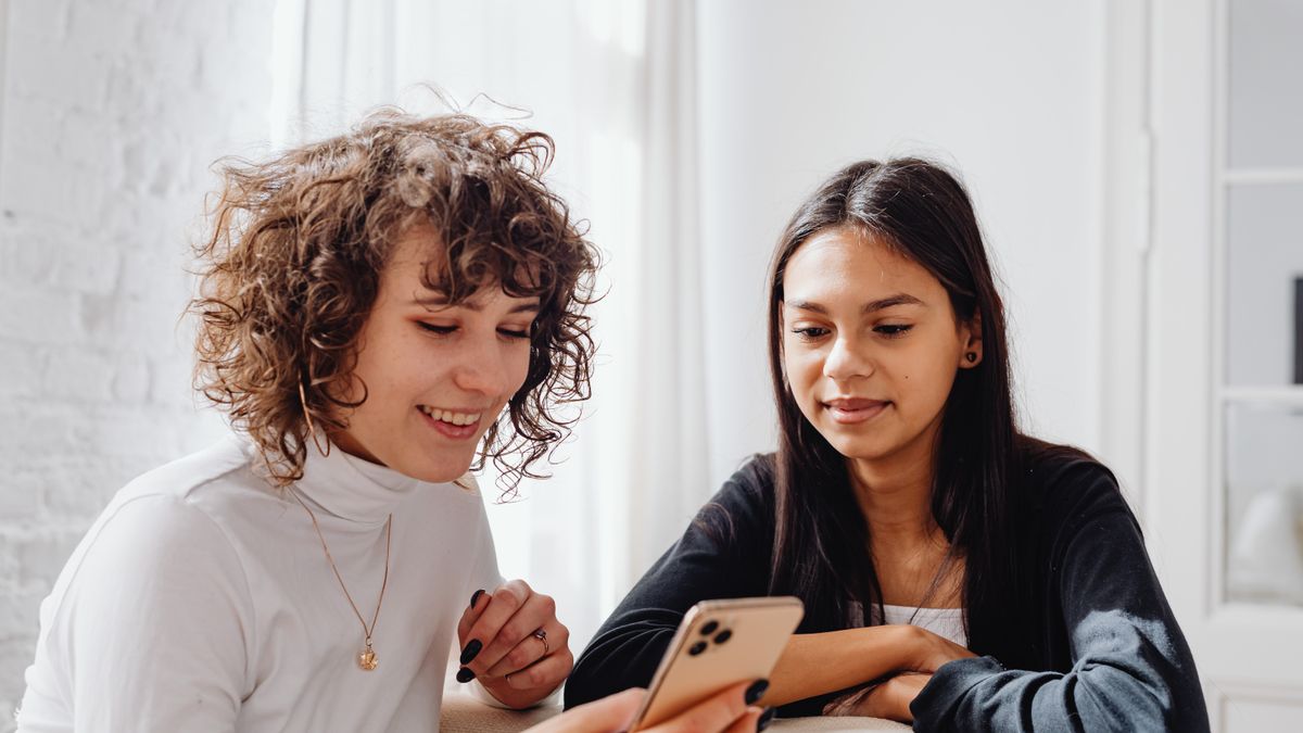 Two young women enjoying a moment together indoors while sharing content on a smartphone.