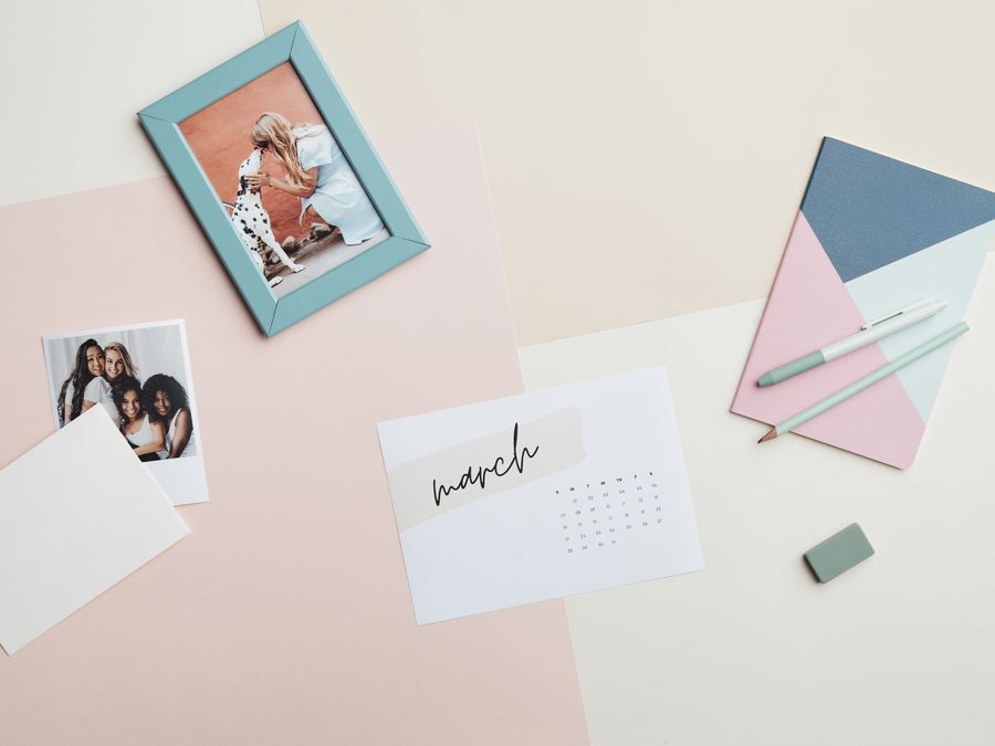 A creative flat lay featuring a calendar, stationery, and photos evoking a clean and organized workspace.