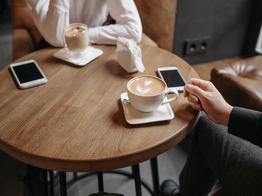 Two people enjoying coffee at a round wooden table indoors with smartphones.