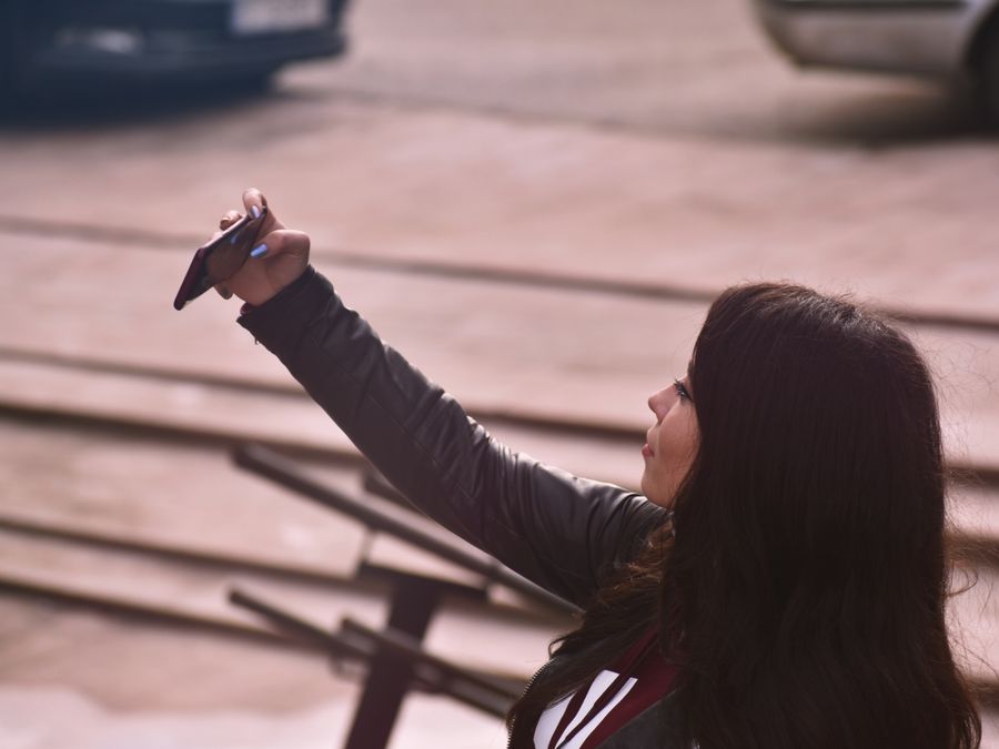 A young woman takes a selfie with her smartphone in an outdoor setting, capturing a moment of joy.